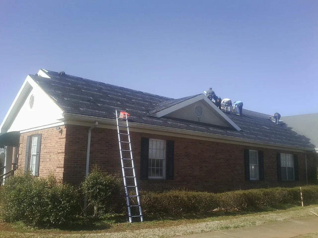 Crew tearing shingles off a brick ranch roof with a ladder set — Metal Roof Repair work by our crew in Kankakee