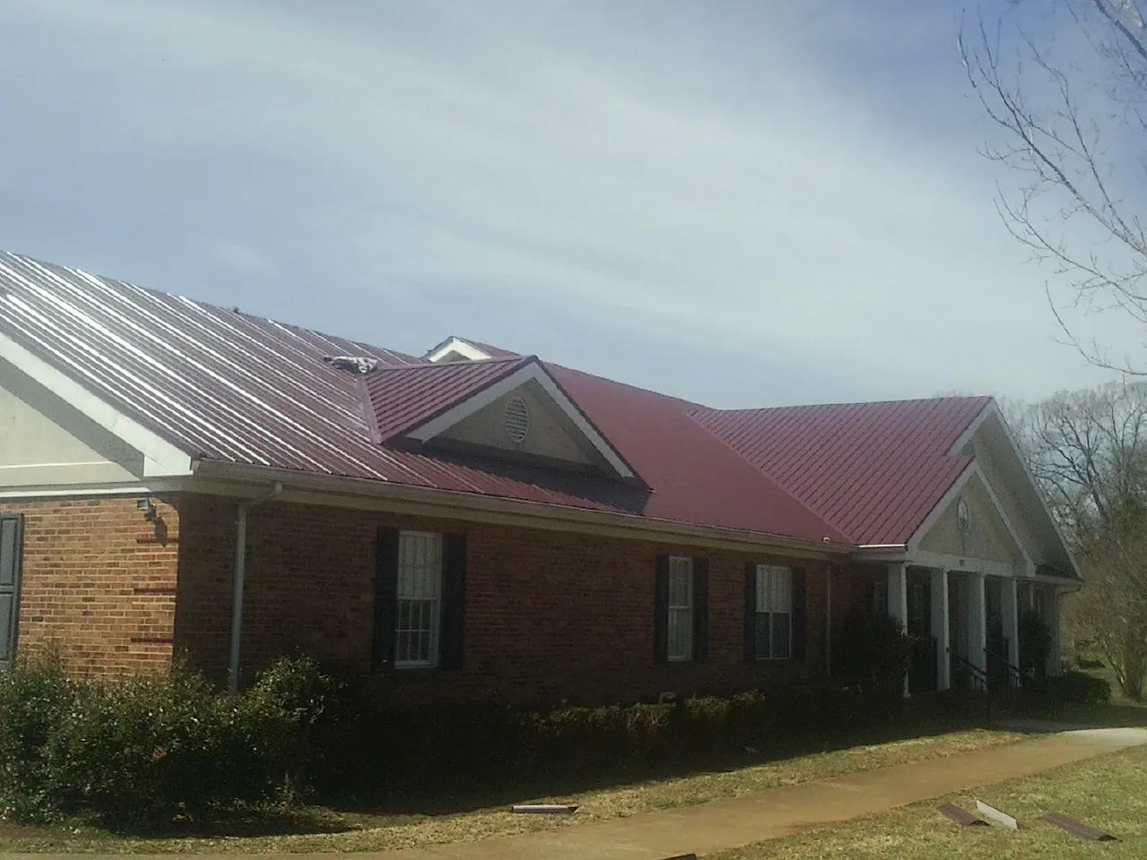 Red metal roof with gabled entries on a long brick building, from a Hail Damage Roof Repair job in Kankakee