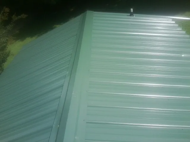 New green metal panels meeting at the ridge of a roof — Flat Roof Repair work by our crew in Kankakee